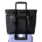 A black roll-top duffel bag with an extended black telescoping handle, shown resting on top of a lavender hard-shell suitcase against a plain white background.