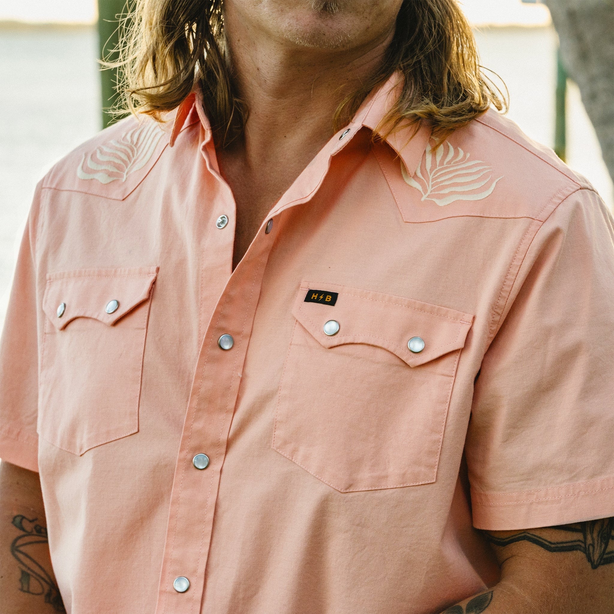 Model wearing Howler Brothers Crosscut Deluxe Snapshirt in Seagrass Coral Oxford outdoors