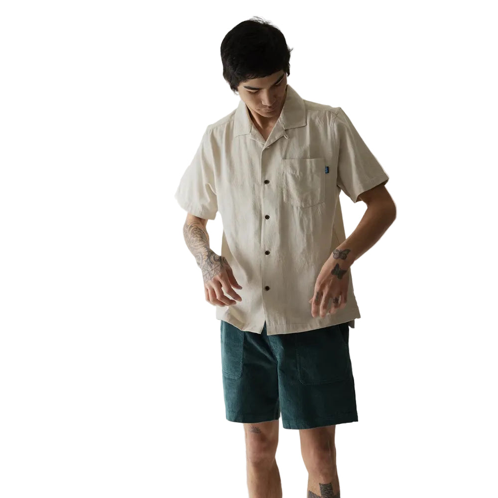 Full-body view of a man wearing the KAVU Deckhouse Short Sleeve Shirt in Tropical Sands for travel, resort wear, and casual summer adventures