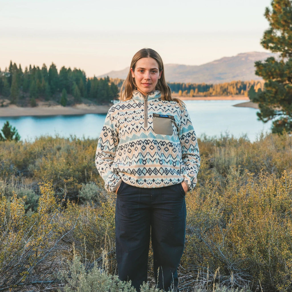 Woman wearing KAVU Women's Hidden Hills Fleece Pullover in Horizon Holiday outdoors by a mountain lake