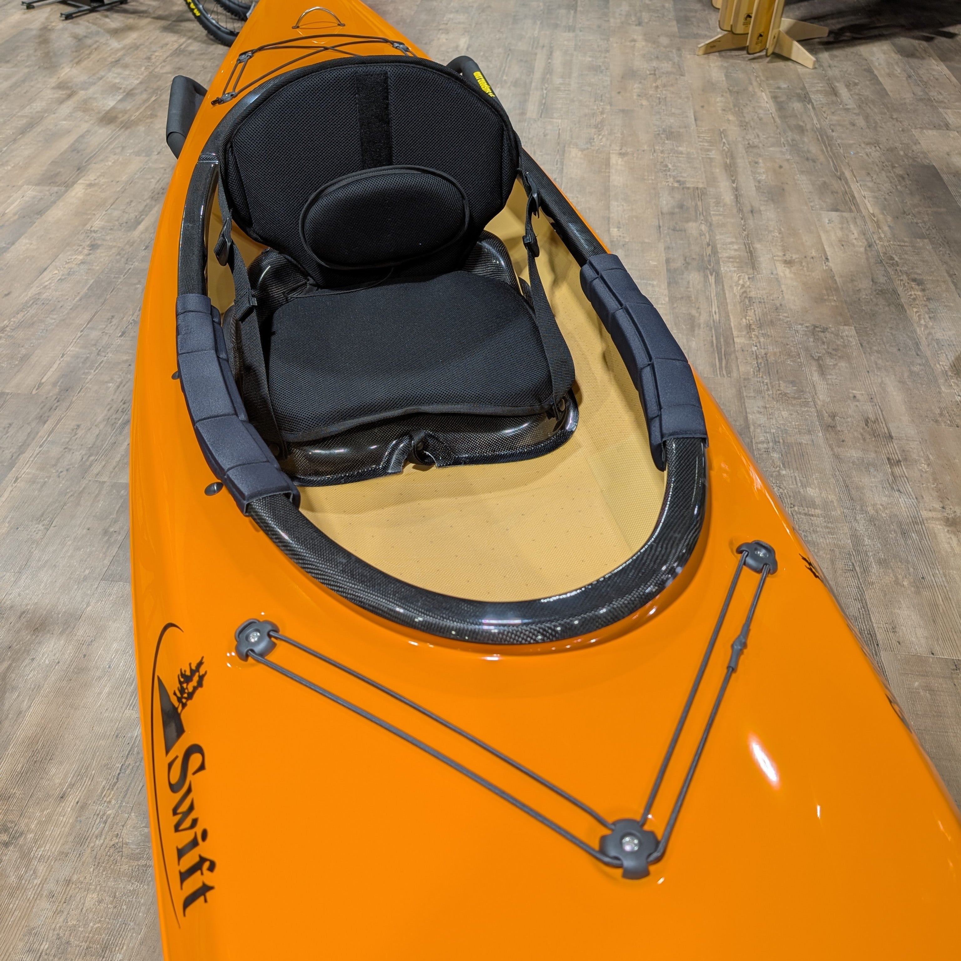 Orange kayak with a black seat on a wooden floor