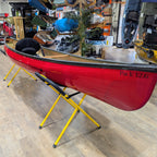 Red kayak on a yellow stand in a store setting with various items in the background