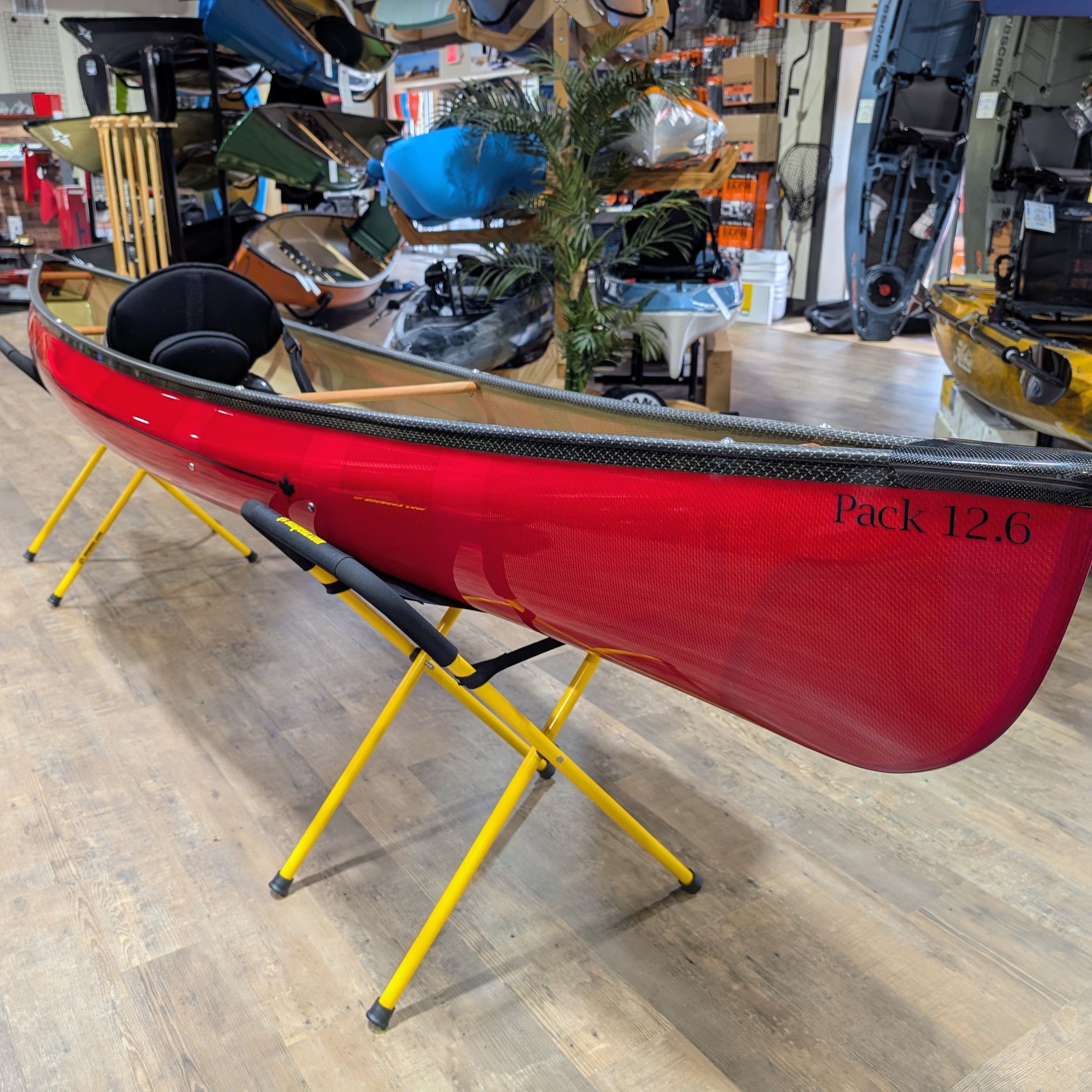 Red kayak on a yellow stand in a store setting with various items in the background